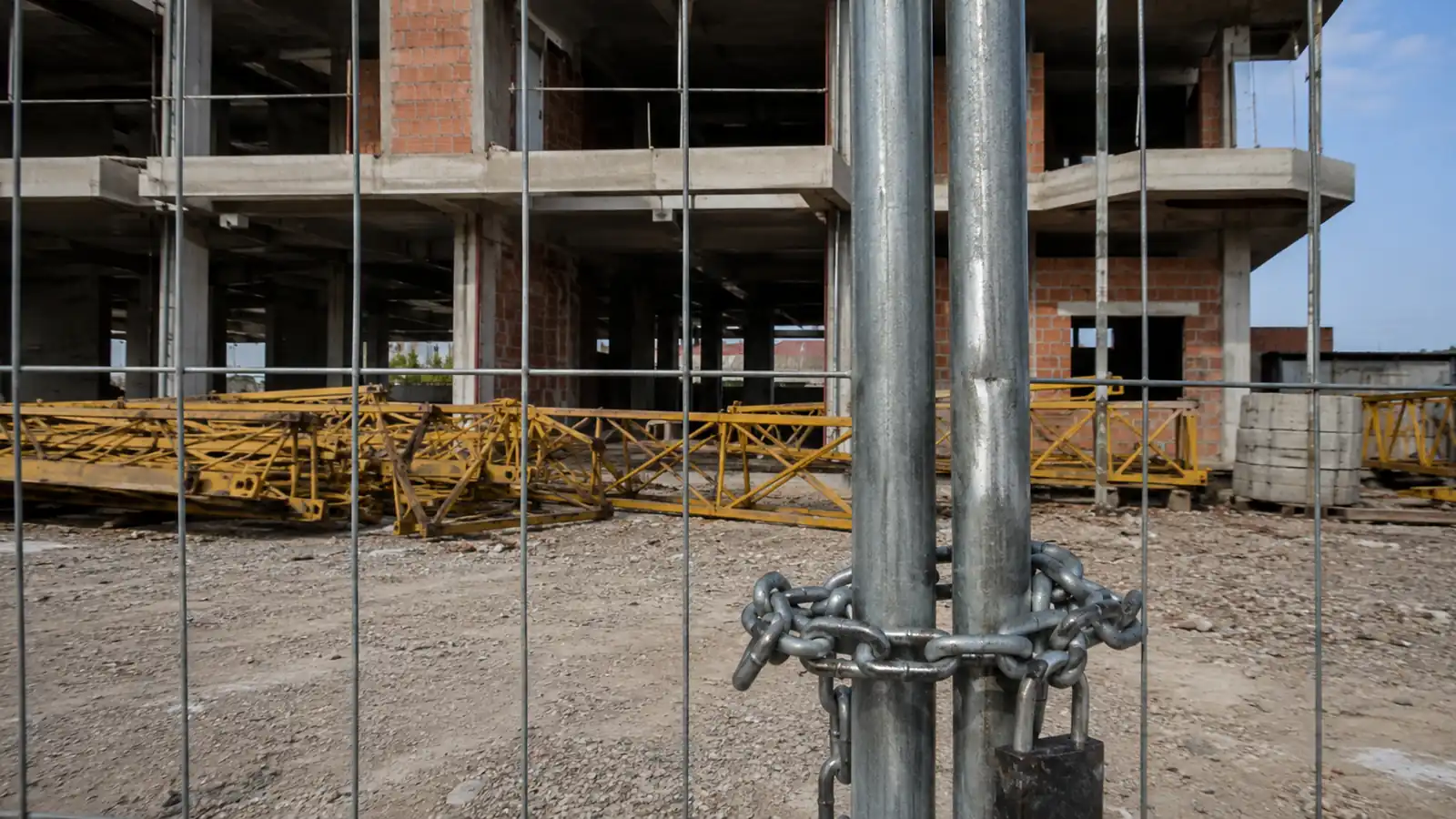 Cantiere residenziale fermo con edificio al grezzo e gru smontata, recinzione chiusa con catena