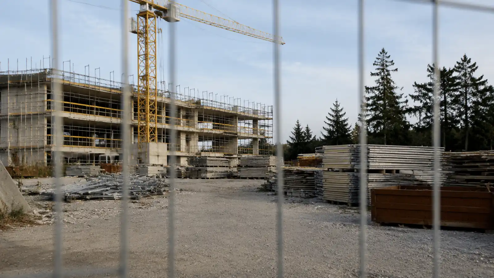 Cantiere edile fermo con gru e materiali accatastati, cancello chiuso con lucchetto e cartello di cantiere sbiadito