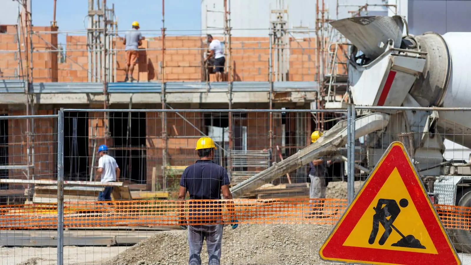Cantiere edile con squadra di operai al lavoro e cartello di cantiere in primo piano