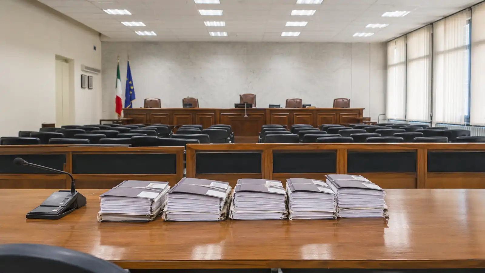 Aula del tribunale amministrativo con banchi vuoti e fascicoli di gara impilati sul tavolo dei difensori