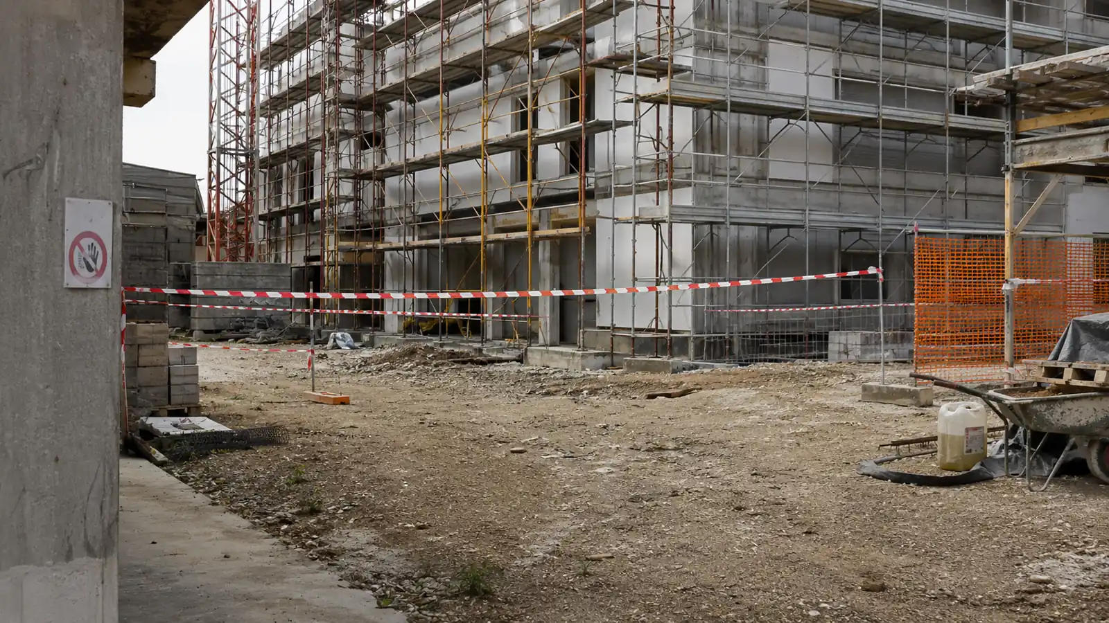 Cantiere edile con area delimitata da nastro bianco e rosso dopo un infortunio, ponteggio sullo sfondo