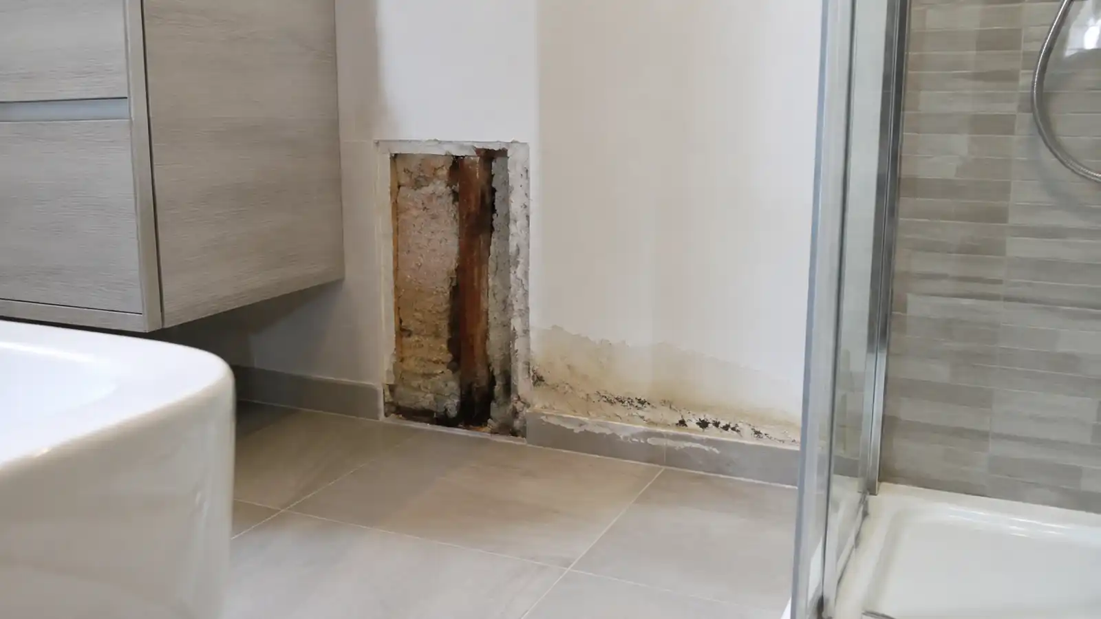 Bagno ristrutturato da poco con piastrelle rimosse in un angolo e macchia di umidità alla base della parete